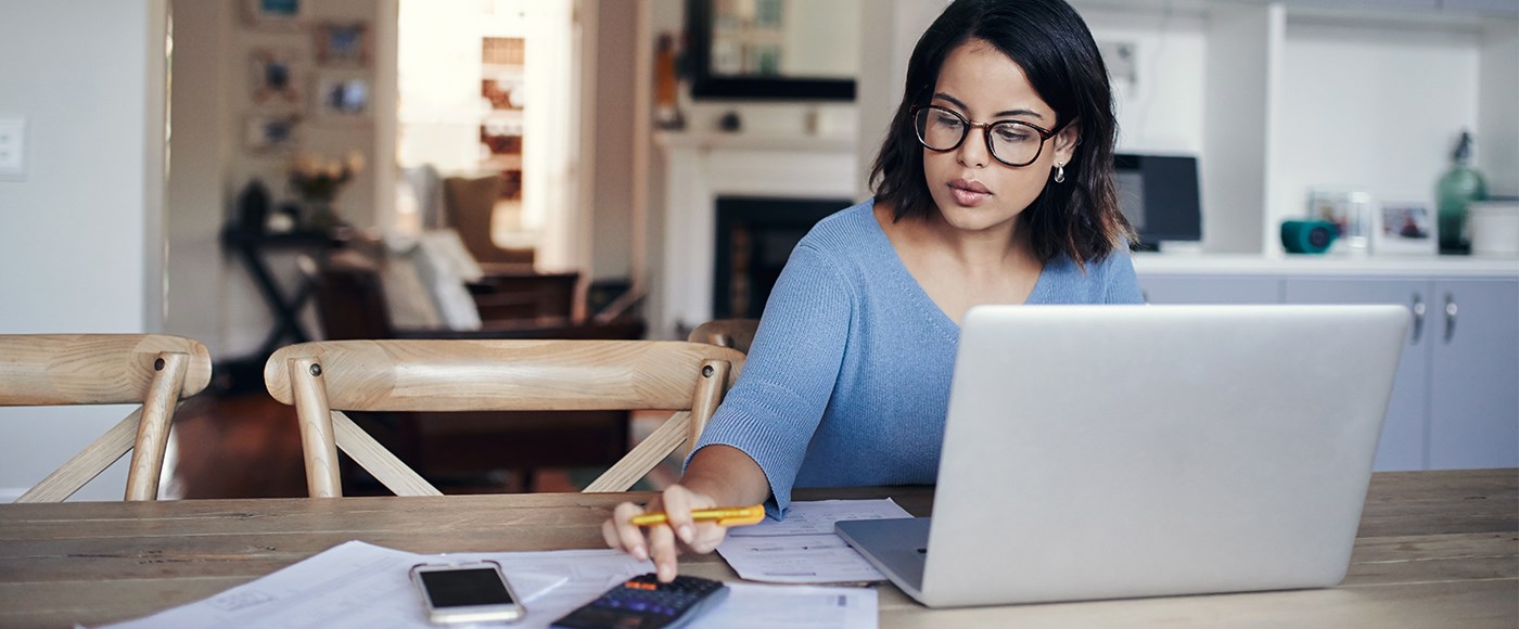 Stock image of someone reviewing their financial plans at a laptop with a calculator nearby.