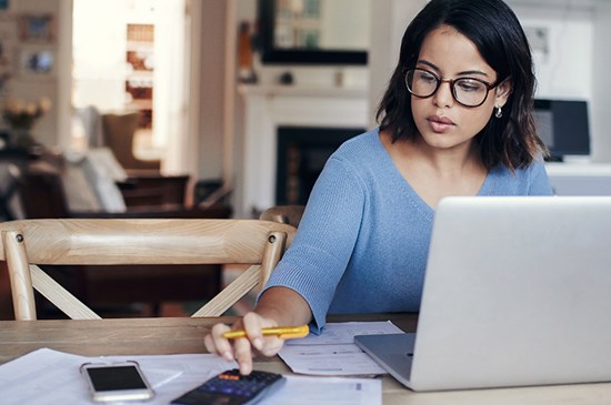 Stock image of someone reviewing their financial plans at a laptop with a calculator nearby.