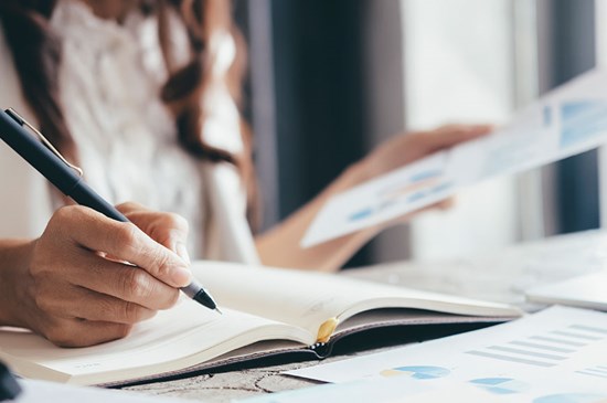 Stock photo of an investor making notes while observing a chart.