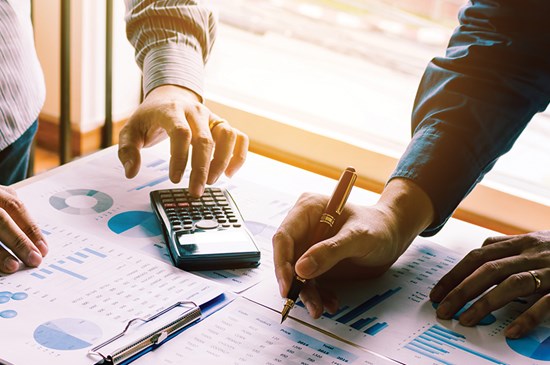 Stock photo showing a calculator with charts and pens displayed on a desk.