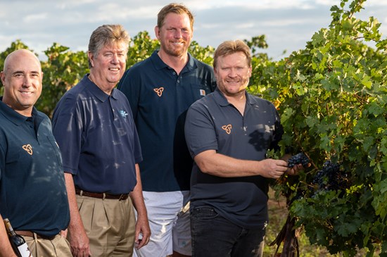 Leadership from Flying Leap vineyards posing for a photo among the grapevines in the vineyard