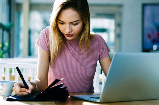 Stock image of a young woman at a desk with a laptop and coffee cup.