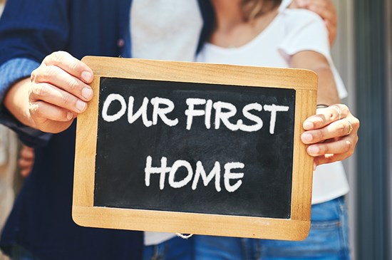 Stock image of a couple holding a sign that reads "our first home"