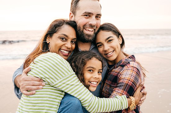 Stock photo of a family hugging and smiling at the camera on a beach