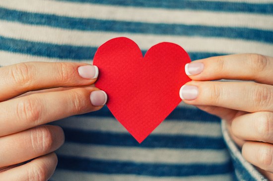 Stock image of a woman's hands holding a cut out paper heart.