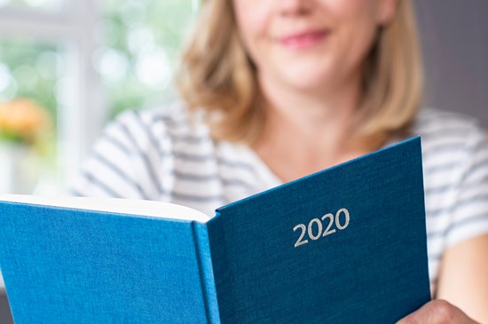 Stock photo of someone reading a book marked "2020" on the front cover.