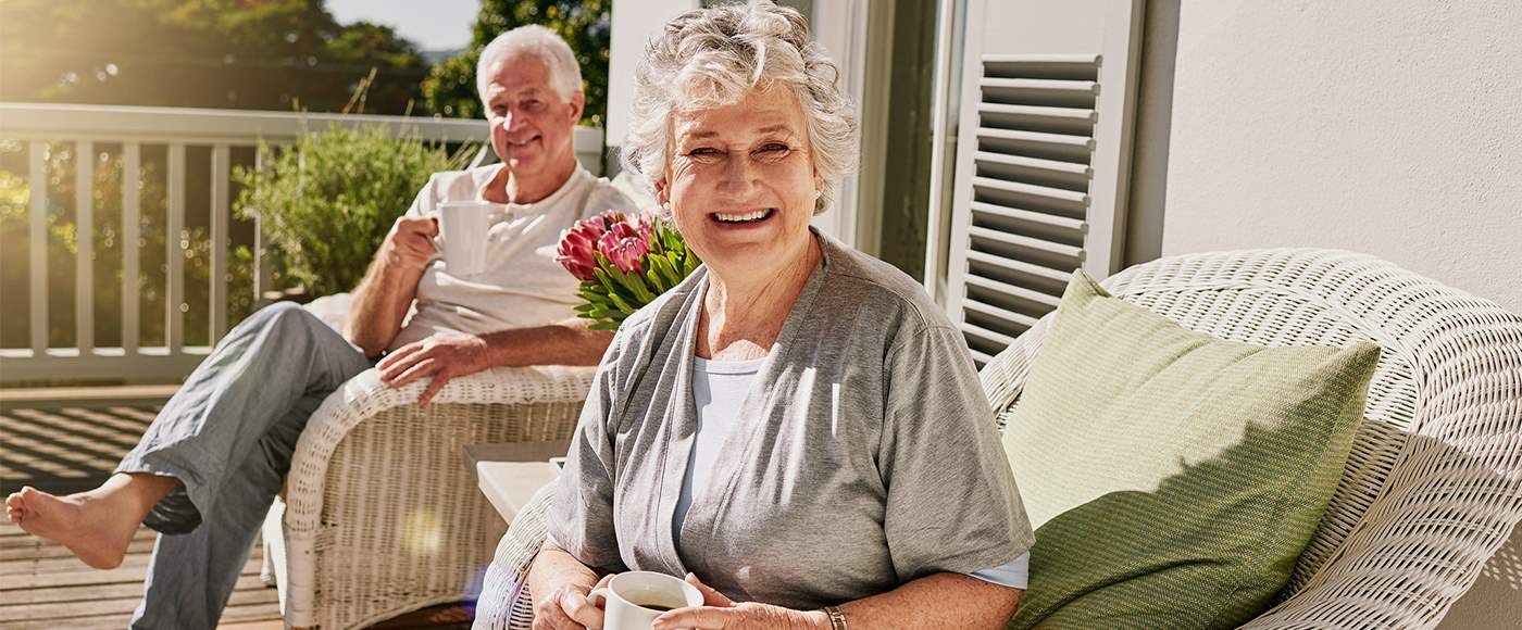 Stock image of two older persons sipping coffee on a front porch.