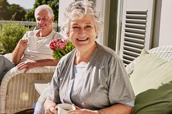 Stock image of two older persons sipping coffee on a front porch.