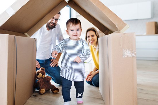 A young family playing with a toddler under a box at home.