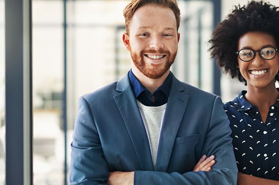 Stock photo of two young professionals smiling at the camera in office attire.
