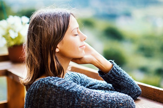 Stock image of a young woman outside breathing fresh air on a wooden deck near a forest.