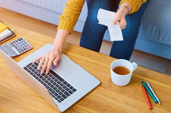 Stock photo of someone working at a laptop on a desk with a calculator and cup of coffee.